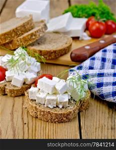 Slices of bread with feta cheese, tomato and dill, napkin on wooden board