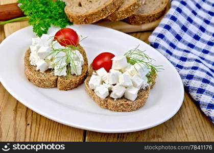 Slices of bread with feta cheese, tomato and dill on a plate, napkin on the background of wooden boards