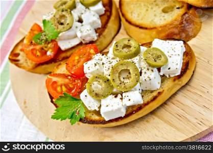 Slices of bread with feta, tomato and olives on a round board, parsley and tomatoes on a background of linen tablecloths