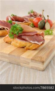 slices of bread with Spanish jamon serrano on a wooden board