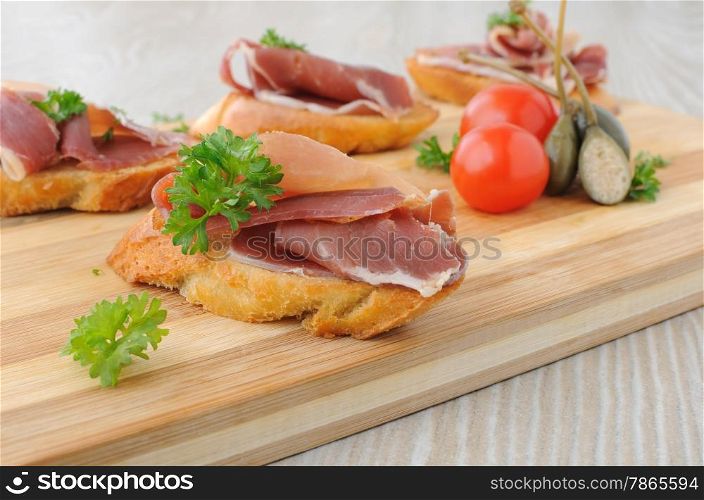 slices of bread with Spanish jamon serrano on a wooden board