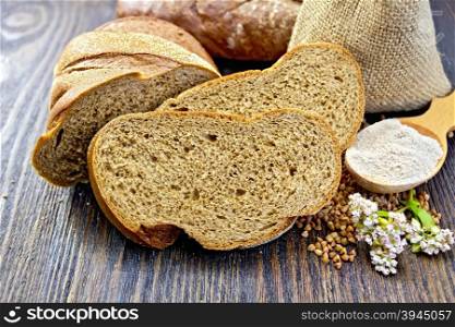 Slices of buckwheat bread, a bag of buckwheat, buckwheat flour in a spoon, flower buckwheat on a background of wooden planks