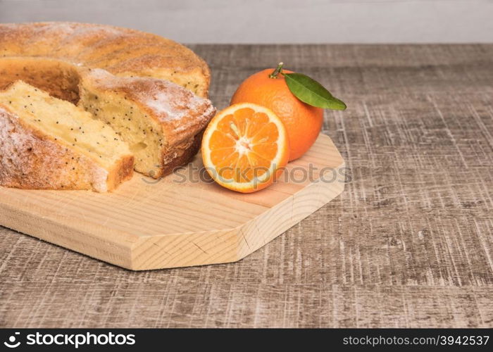 Slices of clementine cake with powdered sugar topping. Cake on a board with fresh clementines on wooden board.