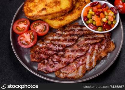 Slices of delicious grilled bacon with croutons fried in egg with spices, salt, vegetables and herbs against a dark concrete background. Slices of delicious grilled bacon with croutons fried in egg with spices, salt, vegetables and herbs