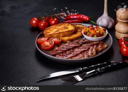 Slices of delicious grilled bacon with croutons fried in egg with spices, salt, vegetables and herbs against a dark concrete background. Slices of delicious grilled bacon with croutons fried in egg with spices, salt, vegetables and herbs