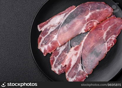 Slices of delicious smoked jamon or prosciutto with salt, spices and herbs on a dark concrete background