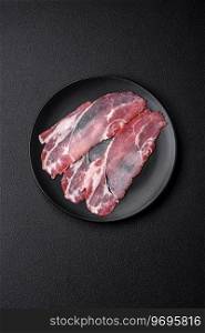 Slices of delicious smoked jamon or prosciutto with salt, spices and herbs on a dark concrete background