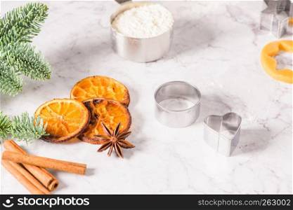 Slices of dried orange and a branch of pine Christmas cookies cutters on marble surface.