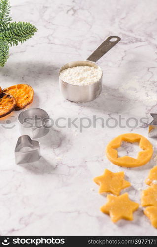 Slices of dried orange and a branch of pine Christmas cookies cutters on marble surface.