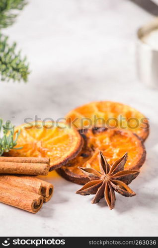 Slices of dried orange and a branch of pine on marble surface.