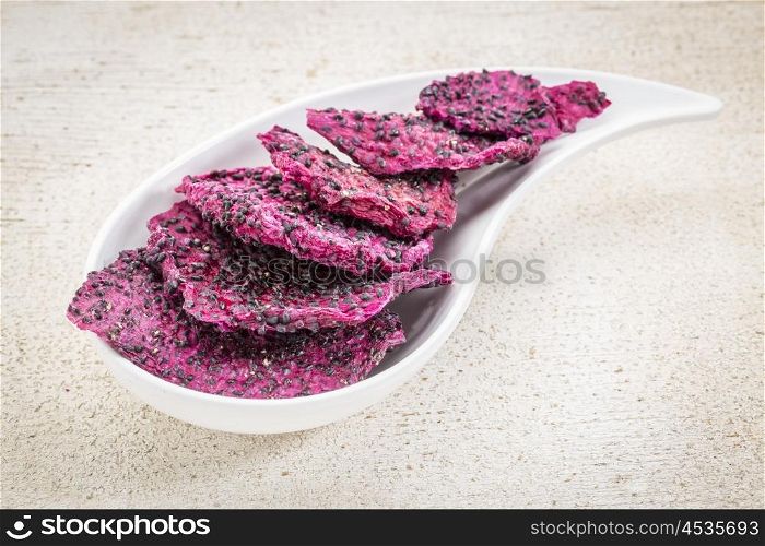 slices of dried red dragon fruit on a teardrop shaped bowl against rustic wood
