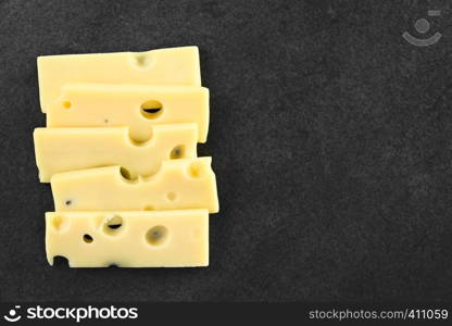 Slices of Emmental, Emmentaler or Emmenthal cheese on slate, photographed overhead with copy space on the right side. Emmental Cheese