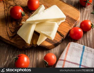 Slices of fresh cheese and tomatos served on wooden plate