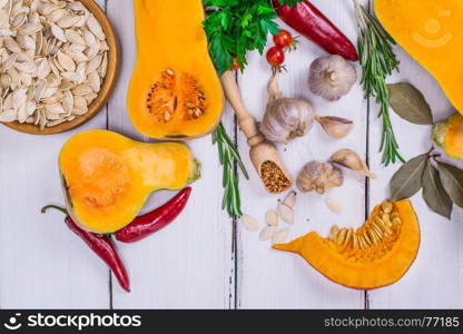 slices of fresh pumpkin and pumpkin seeds with spices for cooking food on a white wooden table, top view