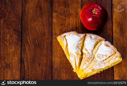Slices of freshly baked apple pie with sugar powder and red apple on a wooden board. Homemade apple cake.