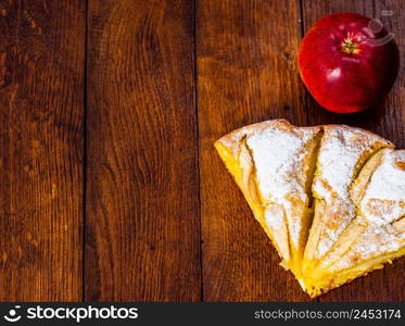 Slices of freshly baked apple pie with sugar powder and red apple on a wooden board. Homemade apple cake.