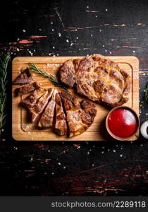 Slices of grilled steak pork on a wooden cutting board. Against a dark background. High quality photo. Slices of grilled steak pork on a wooden cutting board.