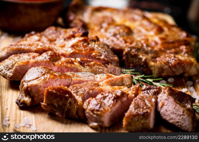 Slices of grilled steak pork on a wooden cutting board. Against a dark background. High quality photo. Slices of grilled steak pork on a wooden cutting board.