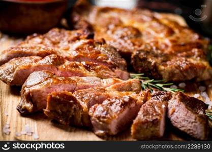 Slices of grilled steak pork on a wooden cutting board. Against a dark background. High quality photo. Slices of grilled steak pork on a wooden cutting board.