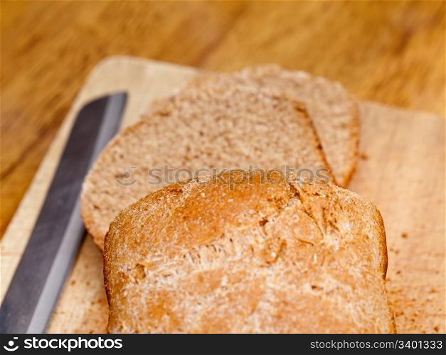Slices of home made wheat bread on breadboard with knife
