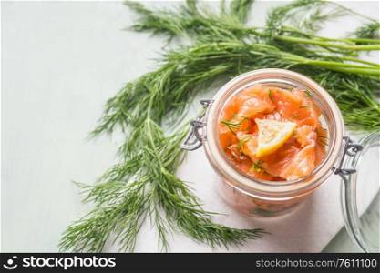 Slices of homemade smoked salmon with dill and lemon in jar on light background. Top view. Healthy food