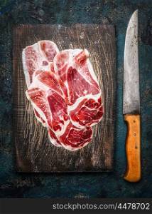 Slices of Iberico ham Cebo with kitchen knife on rustic wooden background, top view.