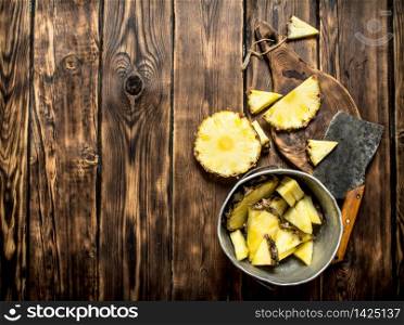 Slices of pineapple in a pot with an axe. On a wooden table.. Slices of pineapple in a pot with an axe.