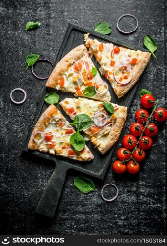 Slices of pizza with tomatoes on a branch and spinach. On dark rustic background. Slices of pizza with tomatoes on a branch and spinach.