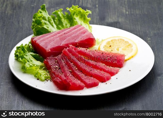 Slices of raw bluefin tuna sashimi on white dish on wood background