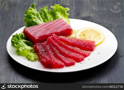 Slices of raw bluefin tuna sashimi on white dish on wood background