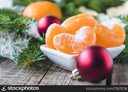 Slices of ripe yellow mandarin lie in a bowl next to the green branches of a Christmas tree and Christmas toys. Citrus fruits, tangerines or oranges.. Slices of ripe yellow mandarin lie in a bowl next to the green branches of a Christmas tree and Christmas toys.