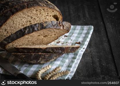 Slices of rye bread fresh baked on a kitchen towel on a black wooden table
