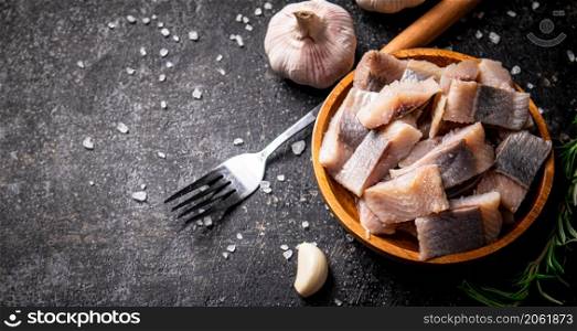 Slices of salted herring on a plate with pieces of salt and a fork. On a black background. High quality photo. Slices of salted herring on a plate with pieces of salt and a fork.