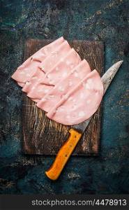 Slices of Sausage Mortadella di Bologna with kitchen knife on rustic wooden background, top view.