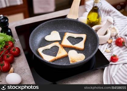 Slices of toast bread with heart shaped holes on frying pan.. Slices of toast bread with heart shaped holes on frying pan