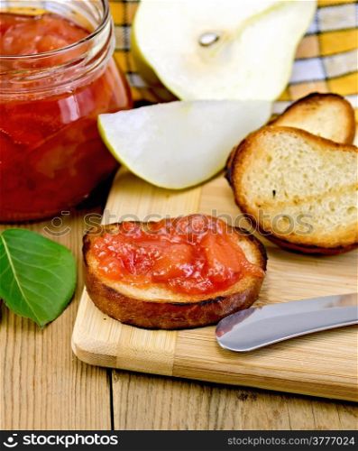 Slices of toasted bread with jam jar of pears, knife, green leaf on a background of wooden boards