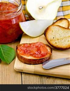 Slices of toasted bread with jam jar of pears, knife, green leaf on a background of wooden boards
