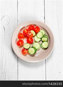 Slices of tomato and cucumbers in a dish. On a white wooden background.. Slices of tomato and cucumbers in a dish.