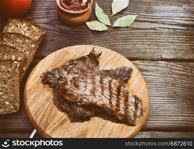 Slices of veal roasted on a grill lie on a wooden board, top view, vintage toning