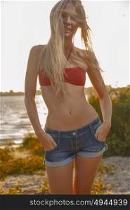 Slim american girl in denim shorts and red bikini on sunset beach