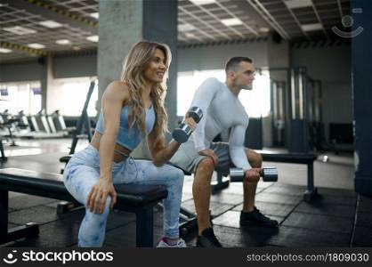 Slim couple doing exercise with dumbbells, fitness training in gym. Athletic man and woman on workout in sport club, active healthy lifestyle, physical wellness. Couple with dumbbells, fitness training in gym