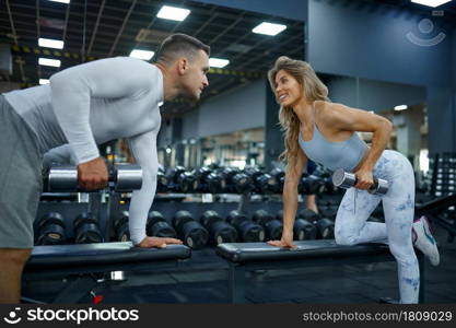 Slim couple doing exercise with dumbbells, training in gym. Athletic man and woman on workout in sport club, active healthy lifestyle, physical wellness. Slim couple doing exercise with dumbbells in gym