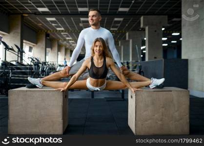 Slim couple doing stretching exercise on cubes in gym. Athletic man and woman on workout in sport club, active healthy lifestyle, physical wellness. Couple doing stretching exercise on cubes in gym