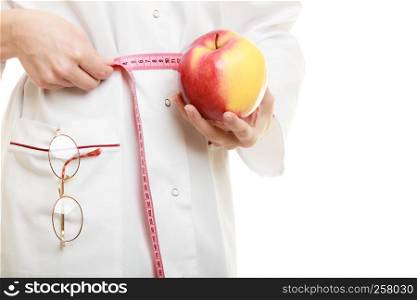 Slim down dieting concept. woman in white lab coat recommending healthy food. Doctor specialist dietitian holding fruit apple measuring her waist isolated.