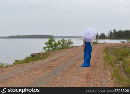 Slim girl in a dress with an umbrella in a forest on a country road
