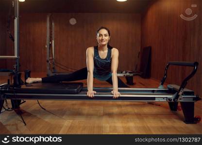 Slim girl in sportswear doing the splits, pilates training on exercise machine in gym. Fitness workuot in sport club. Athletic female person, aerobics indoor, body stretching. Slim girl doing the splits, pilates training