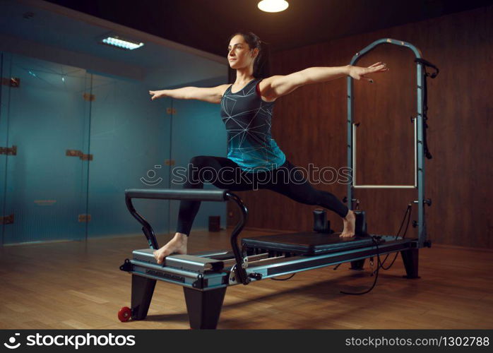 Slim girl in sportswear keeps the balance, pilates training on exercise machine in gym. Fitness workuot in sport club. Athletic female person, aerobics indoor, body stretching. Slim girl keeps the balance, pilates training