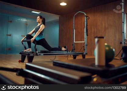 Slim girl in sportswear keeps the balance, pilates training on exercise machine in gym. Fitness workuot in sport club. Athletic female person, aerobics indoor, body stretching. Slim girl keeps the balance, pilates training