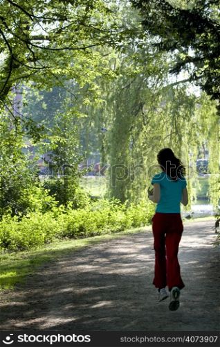 Slim girl running in park under sunlit trees