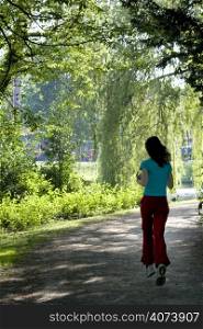 Slim girl running in park under sunlit trees